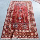 A RED GROUND RUG the design incorporating stylised buildings, 123cm x 212cm