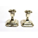 A PAIR OF SILVER DWARF CANDLESTICKS with square cut corner and stepped bases, weighted. Condition