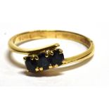 A 14 CARAT YELLOW GOLD RING crossover set with three small blue sapphires, ring size P½, gross