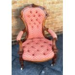 A VICTORIAN CARVED WALNUT FRAMED ARMCHAIR with button upholstered seat and back, on turned