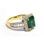 A MODERN EMERALD AND DIAMOND RECTANGULAR CLUSTER RING with drop set shoulders, the emerald