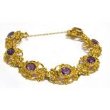 A 9 CARAT GOLD AMETHYST SET BRACELET seven oval openwork links with scroll and flower head