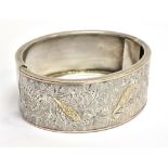 A VICTORIAN SILVER HINGED BANGLE the front with fern and leaf decoration, with three small gold leaf