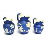 A GRADUATED SET OF THREE WEDGWOOD JASPERWARE JUGS the largest depicting Psyche bound and wounded