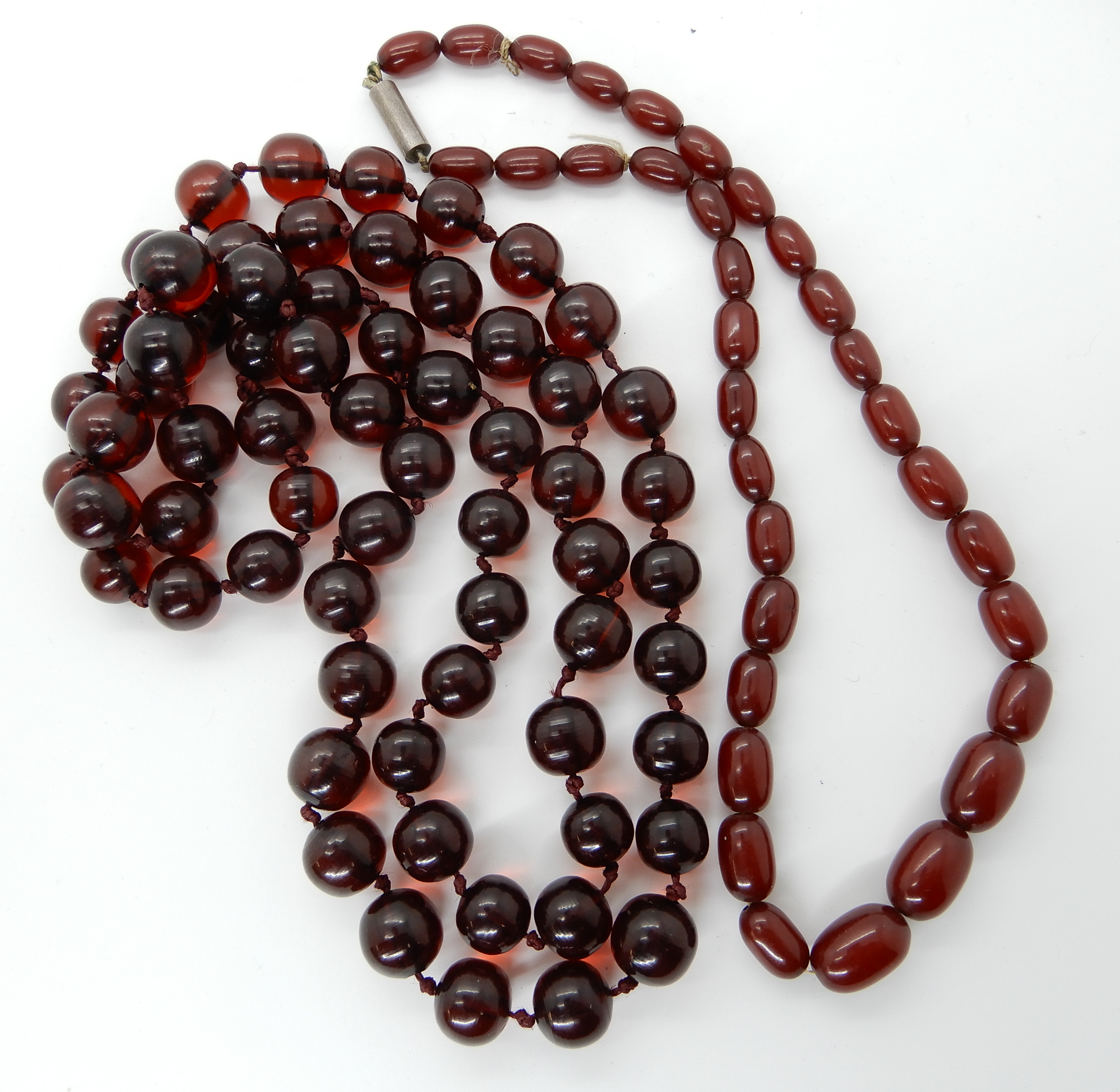 Two strings of cherry amber coloured beads, round beads weight 106.2gms, oval beads weight 25.5gms