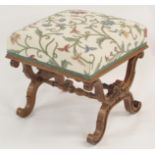 A VICTORIAN WALNUT STOOL with crewelwork padded seat above a carved cross-frame joined by turned
