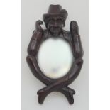 A CONTINENTAL WOODEN FIGURAL MIRROR modelled as a crossed legged man holding a cup in one hand, 49cm