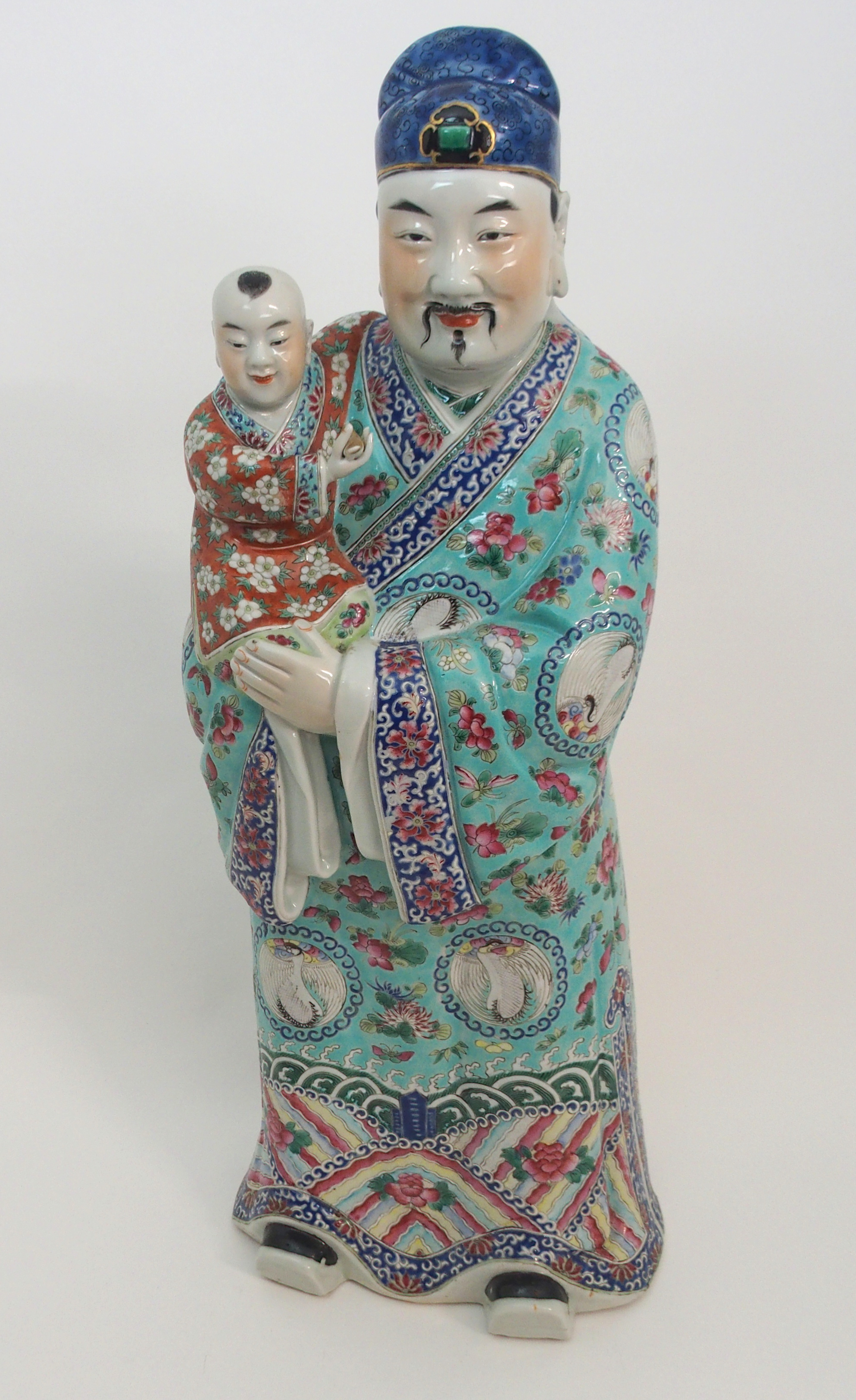 A CANTON FIGURE OF AN OFFICIAL HOLDING A CHILD standing and wearing kimono set with crane roundels