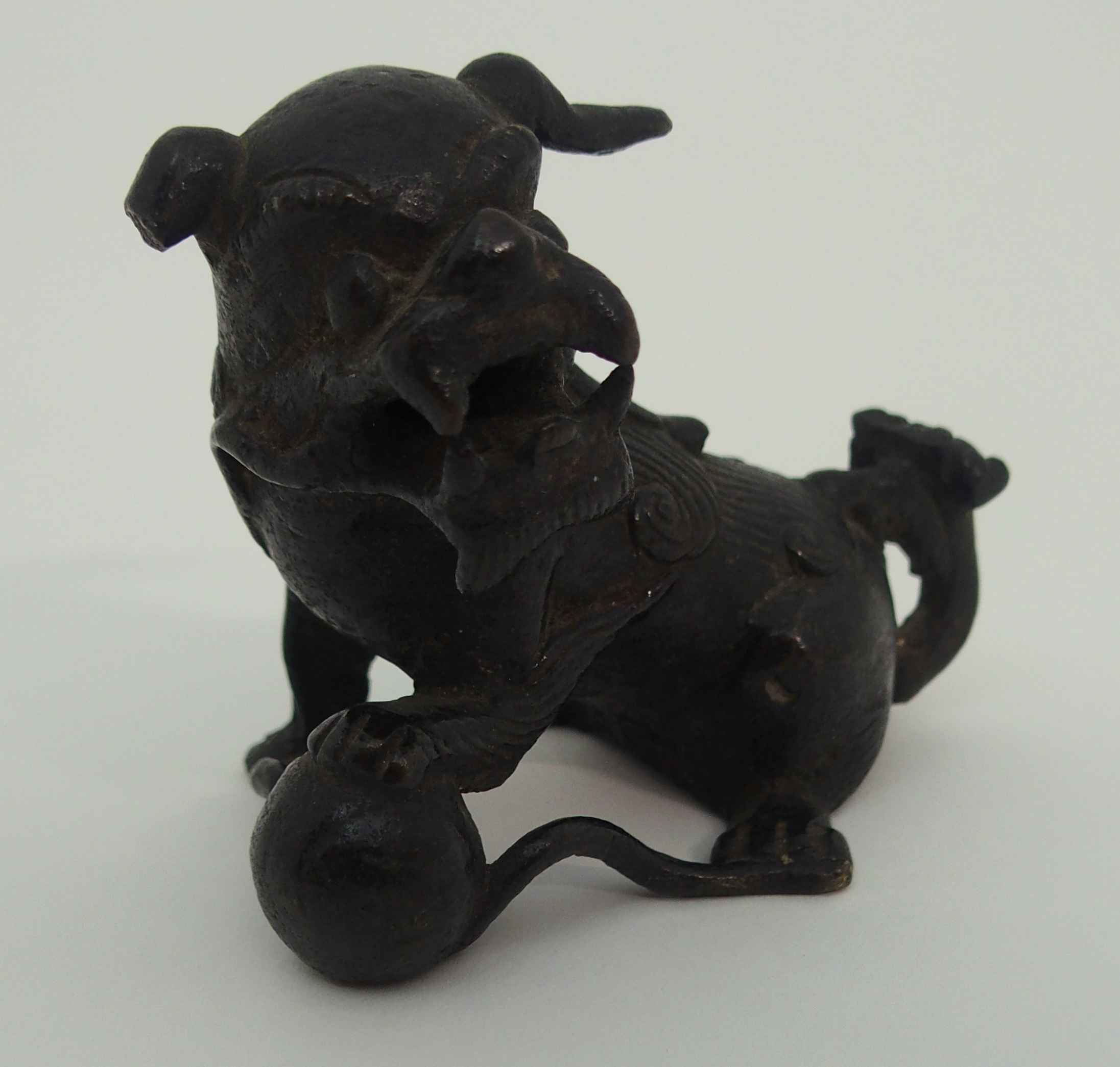 A CHINESE BRONZE SHISHI modelled seated and holding a brocade ball, 17th/18th Century, 6.5cm high