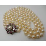 A TRIPLE STRING OF BAROQUE PEARLS with a white metal gem and pearl set flower clasp, length of the