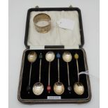 A lot comprising a cased set of silver coffee bean spoons and a white metal napkin ring,