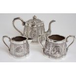 AN ASIAN WHITE METAL THREE PIECE TEA SERVICE cast and decorated with figures in cartouche panels