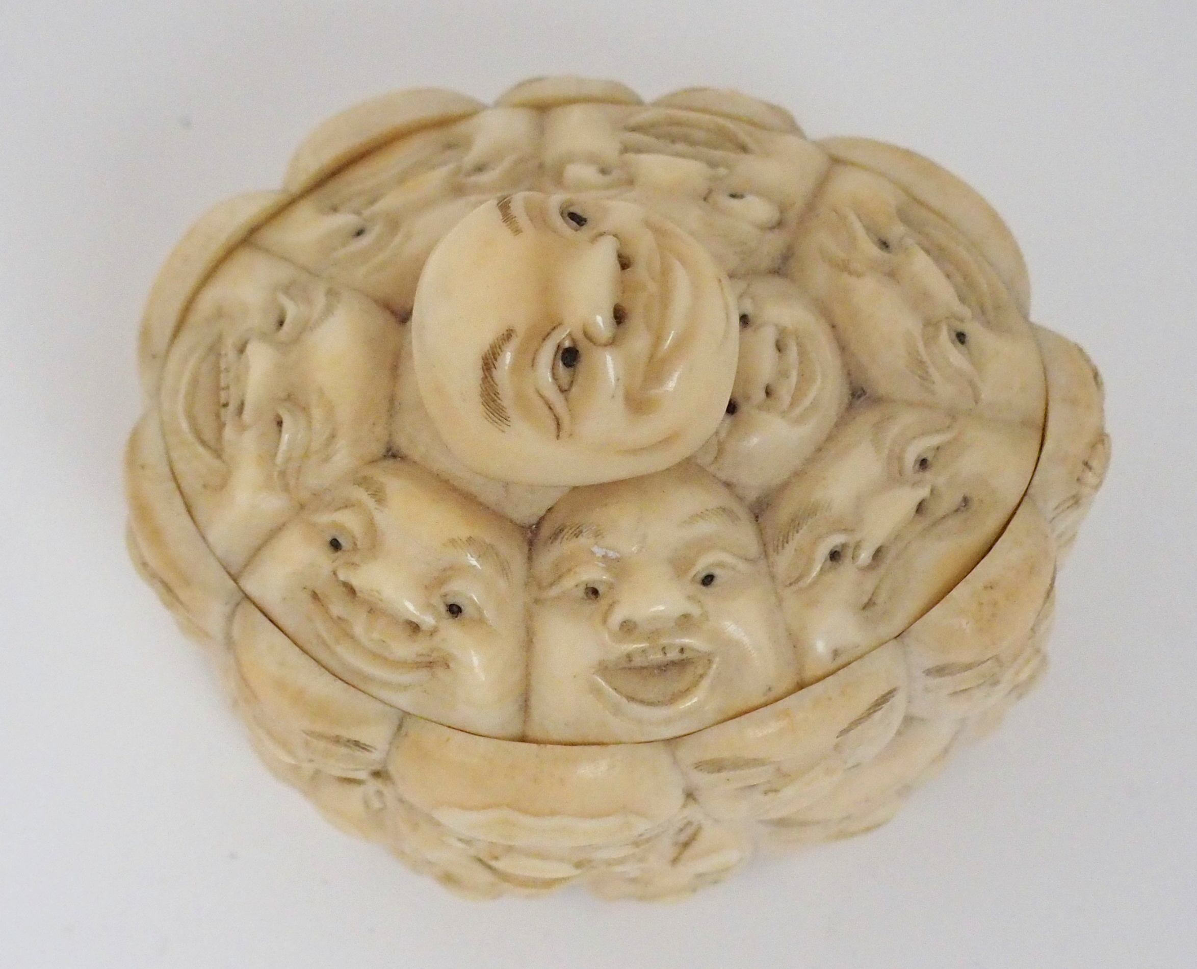 A JAPANESE IVORY OVAL MASK BOX AND COVER carved with many face masks, the cover with mask finial, - Image 8 of 14