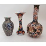 AN IMARI BOTTLE SHAPED VASE painted with figures in gardens surrounded by foliage and detailed in