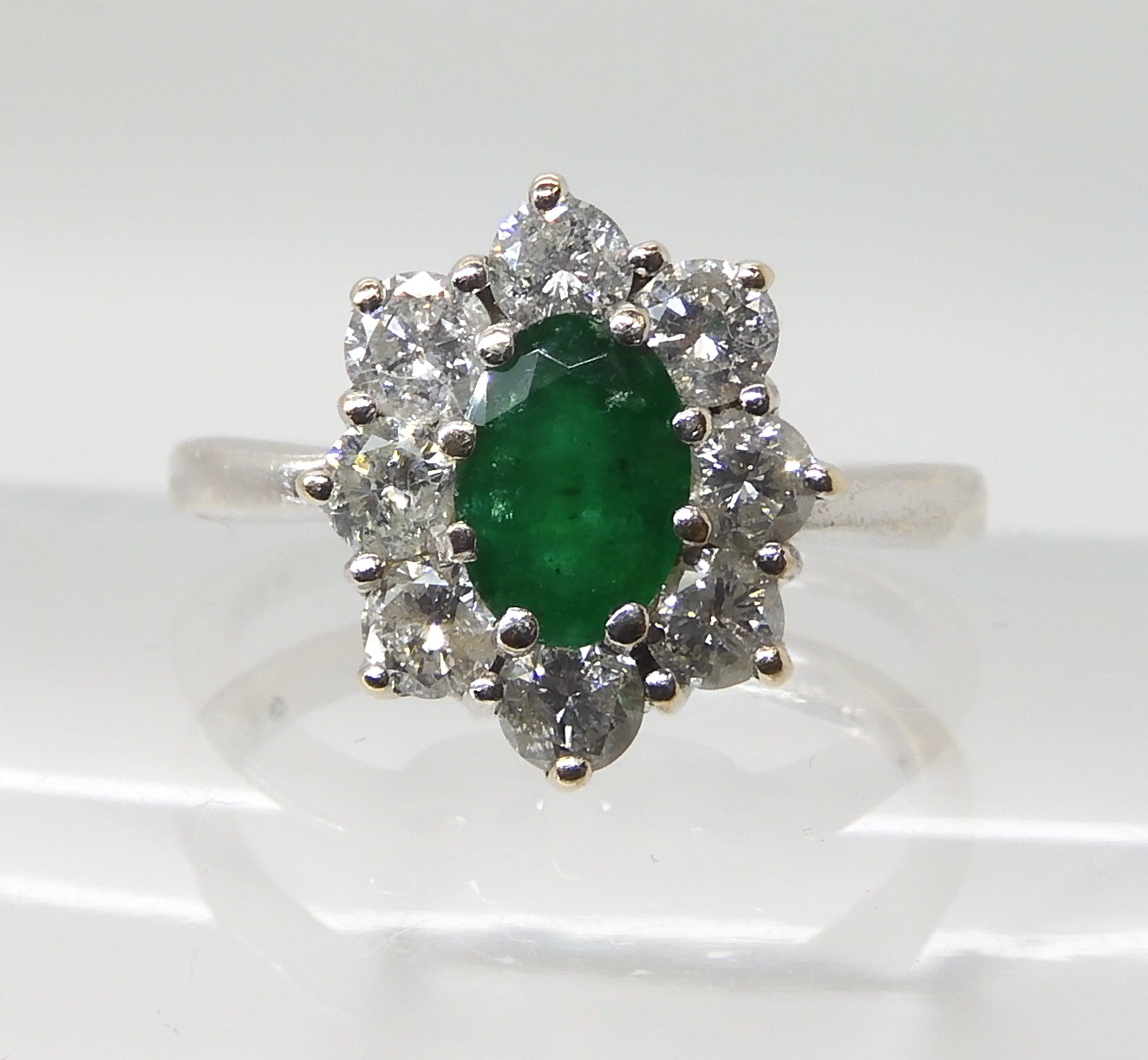 A 9CT WHITE GOLD EMERALD AND DIAMOND CLUSTER RING set with an oval emerald of approx 7mm x 5mm x 3.