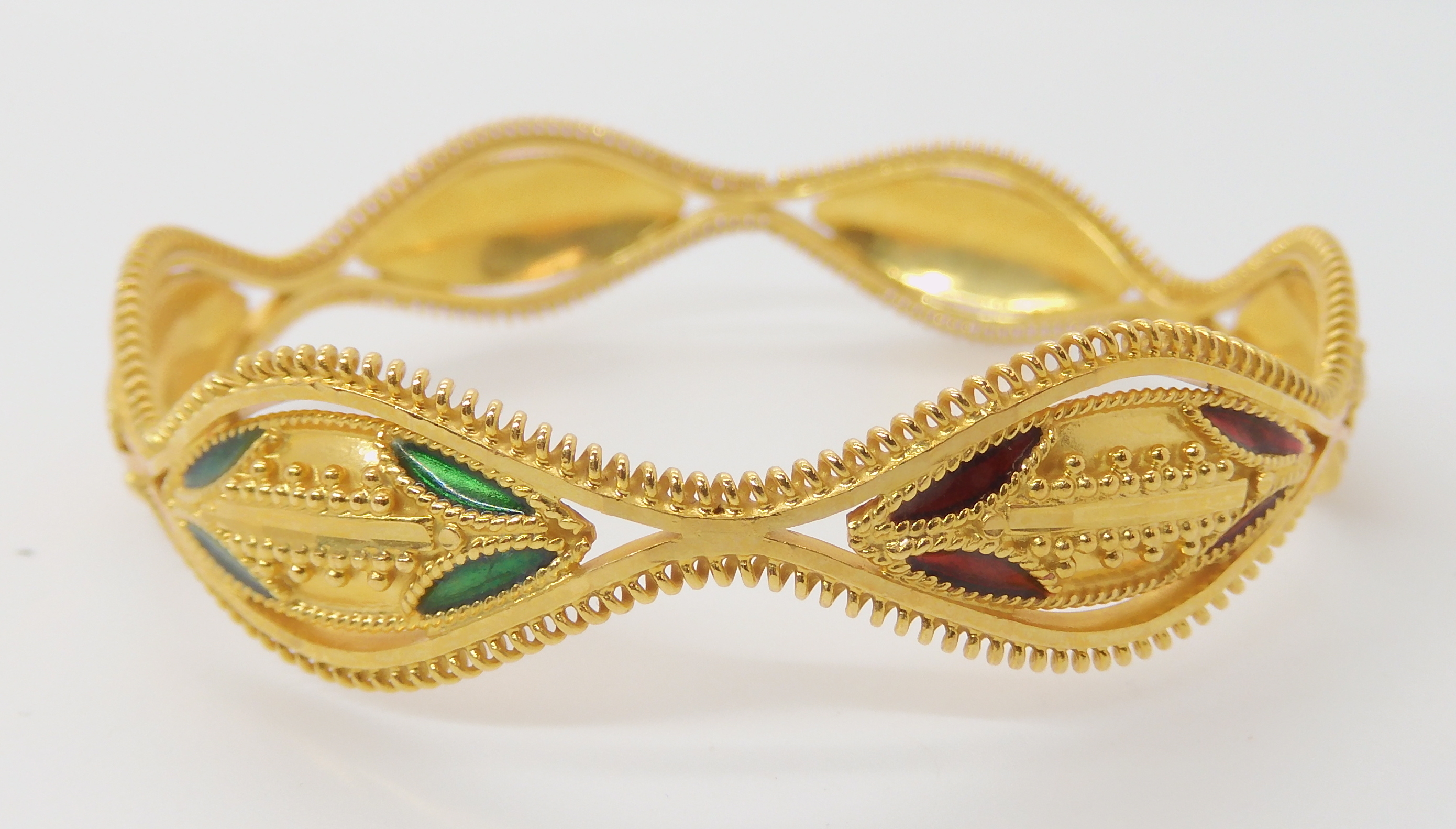 A BRIGHT YELLOW METAL DECORATIVE BANGLE with red and green enamel and granulation detail, stamped