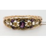 A 9CT GOLD EDWARDIAN GEM SET BANGLE set with seed pearls and purple glass gems, to the decorative