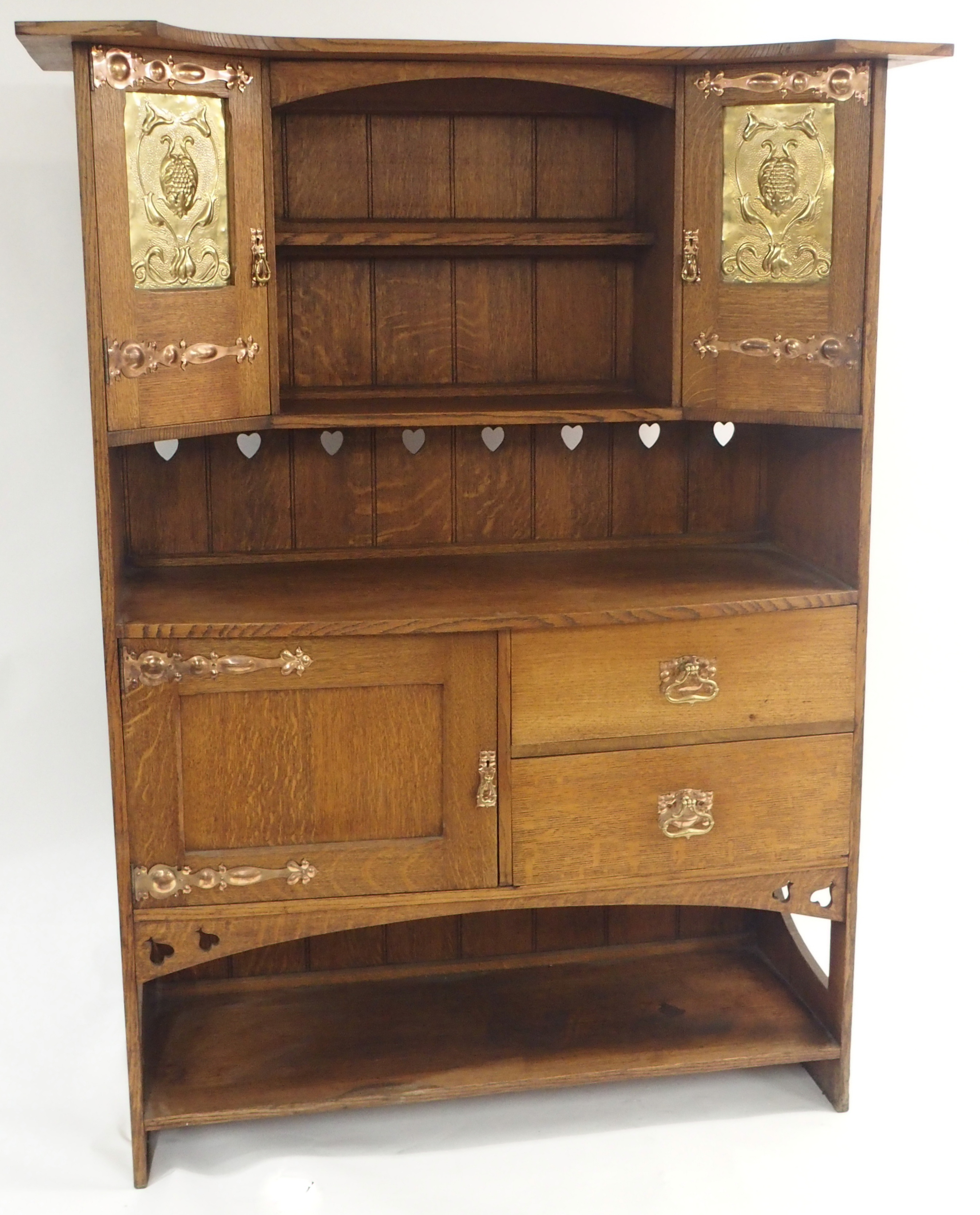 AN ARTS AND CRAFTS OAK DRESSER with open shelves, flanked by embossed inset brass panels and