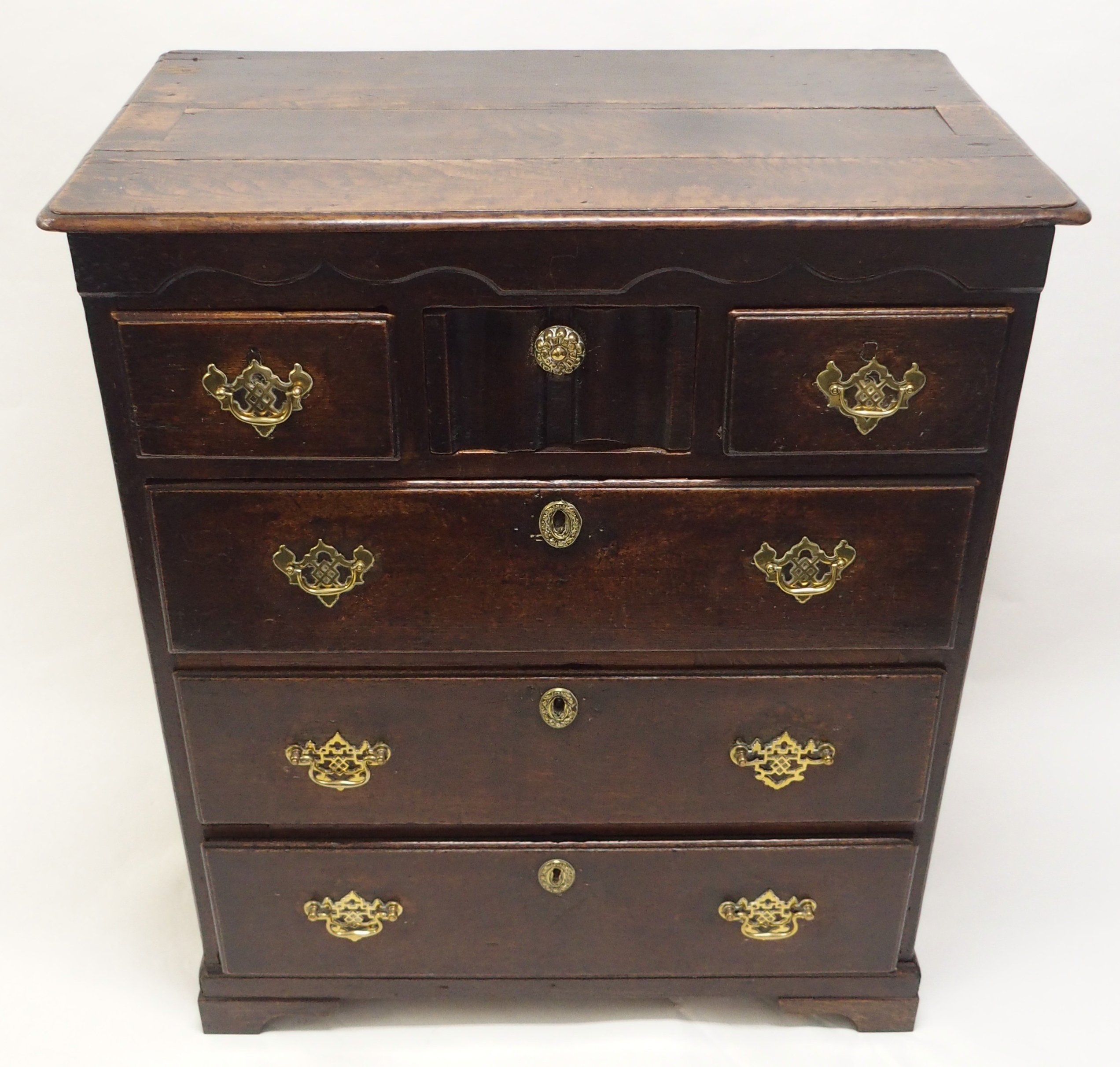 AN 18TH CENTURY OAK CHEST with shaped frieze above a central linen fold drawer, flanked by two short