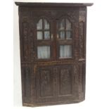 A VICTORIAN STAINED OAK CORNER DISPLAY CABINET carved allover with scrolling foliage, with a pair of