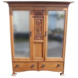 AN OAK ARTS AND CRAFTS WARDROBE the overhanging cornice above a central carved foliate panel and