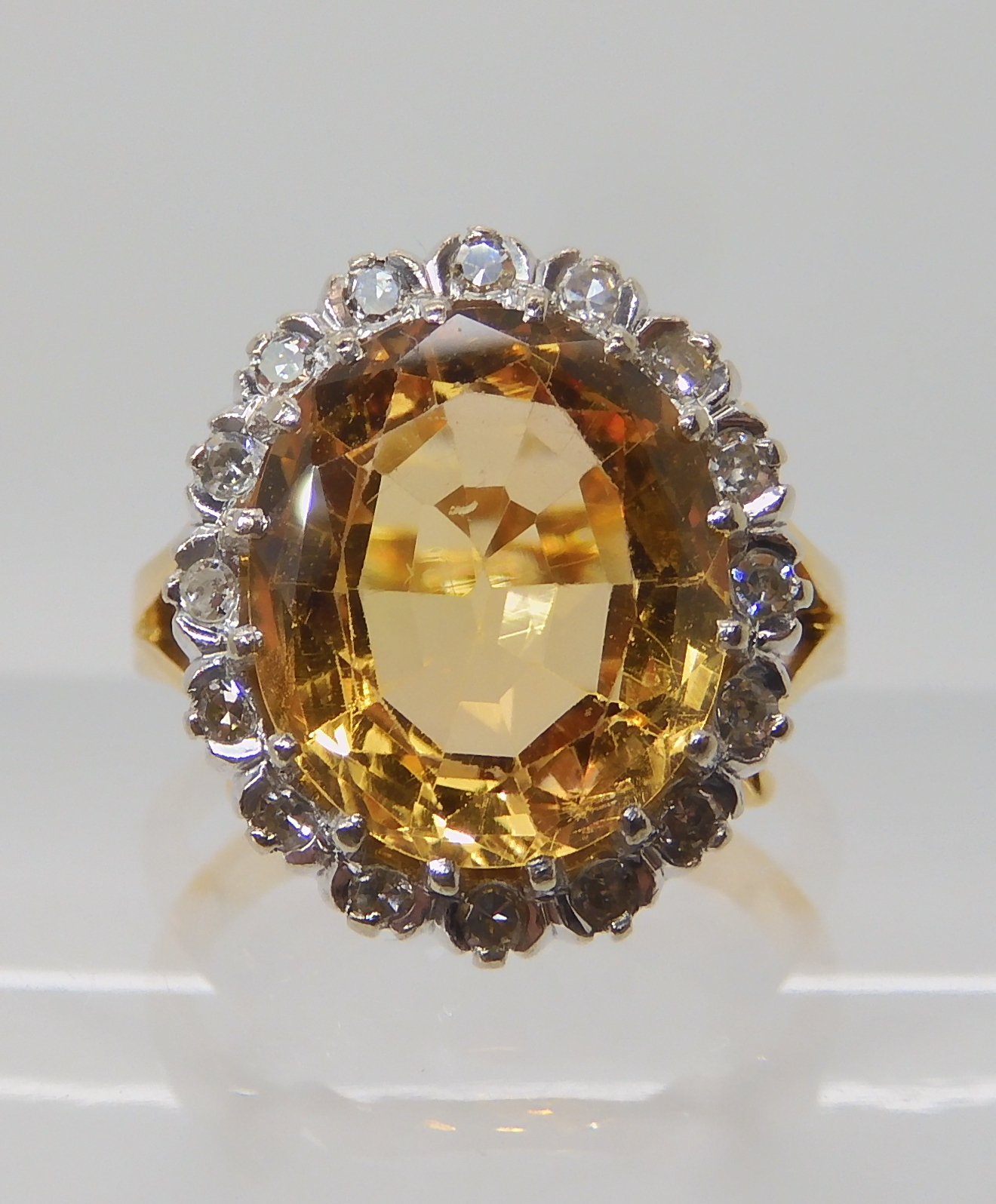 A bright yellow metal ring set with a yellow topaz surrounded with a ring of eight cut diamonds,