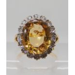 A bright yellow metal ring set with a yellow topaz surrounded with a ring of eight cut diamonds,