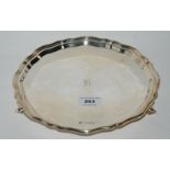 A silver card tray of circular form with scalloped rim on scalloped rim on three scrolling feet,