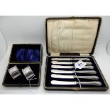 A lot comprising a cased set of six silver handled butter knives and a cased pair of silver napkin