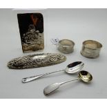 A lot comprising two silver napkin rings, two spoons, a jar lid and a part book cover Condition