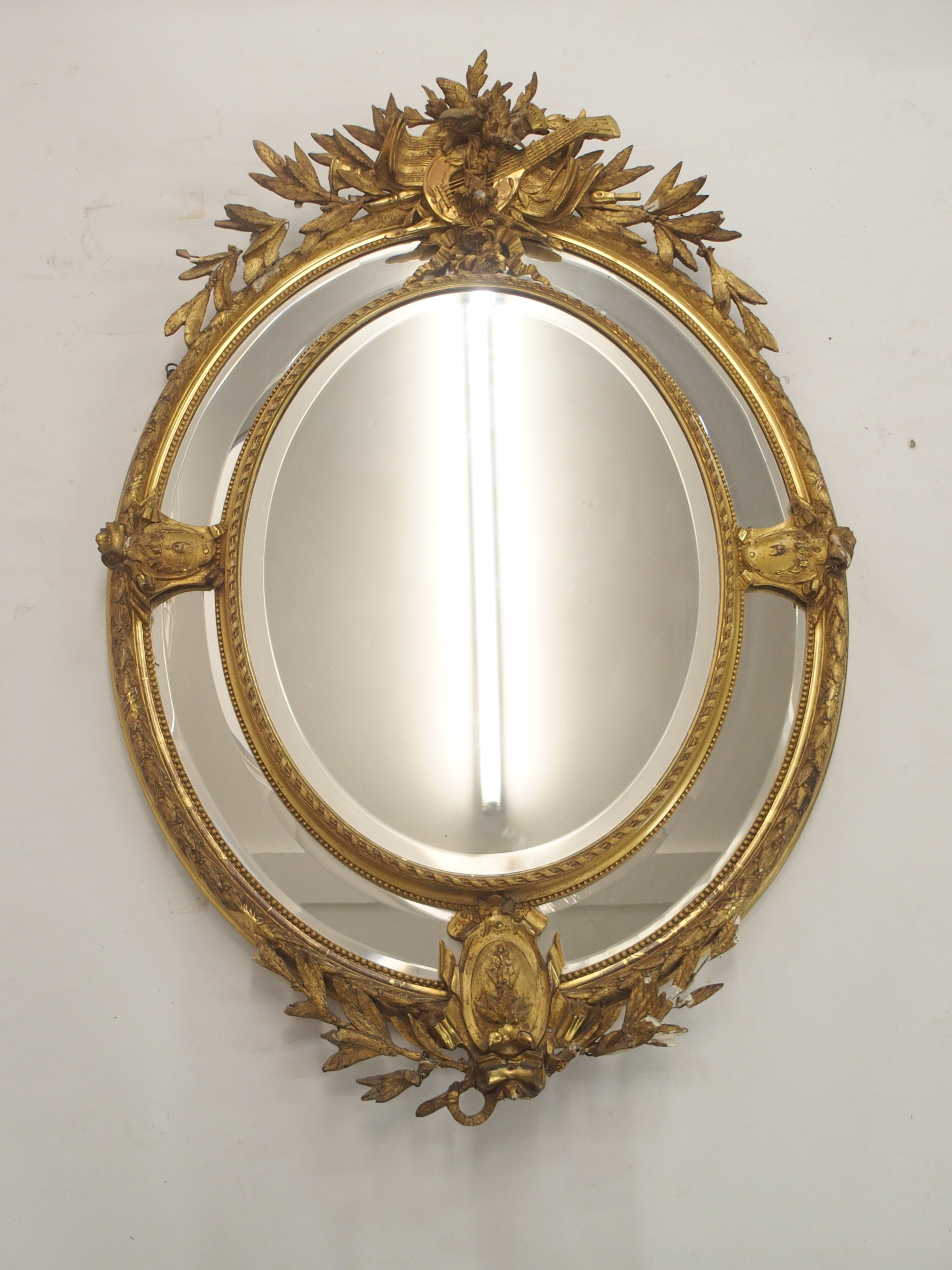 A LOUIS XVI STYLE GILTWOOD AND GESSO OVAL WALL MIRROR with birds and musical trophy surmount above