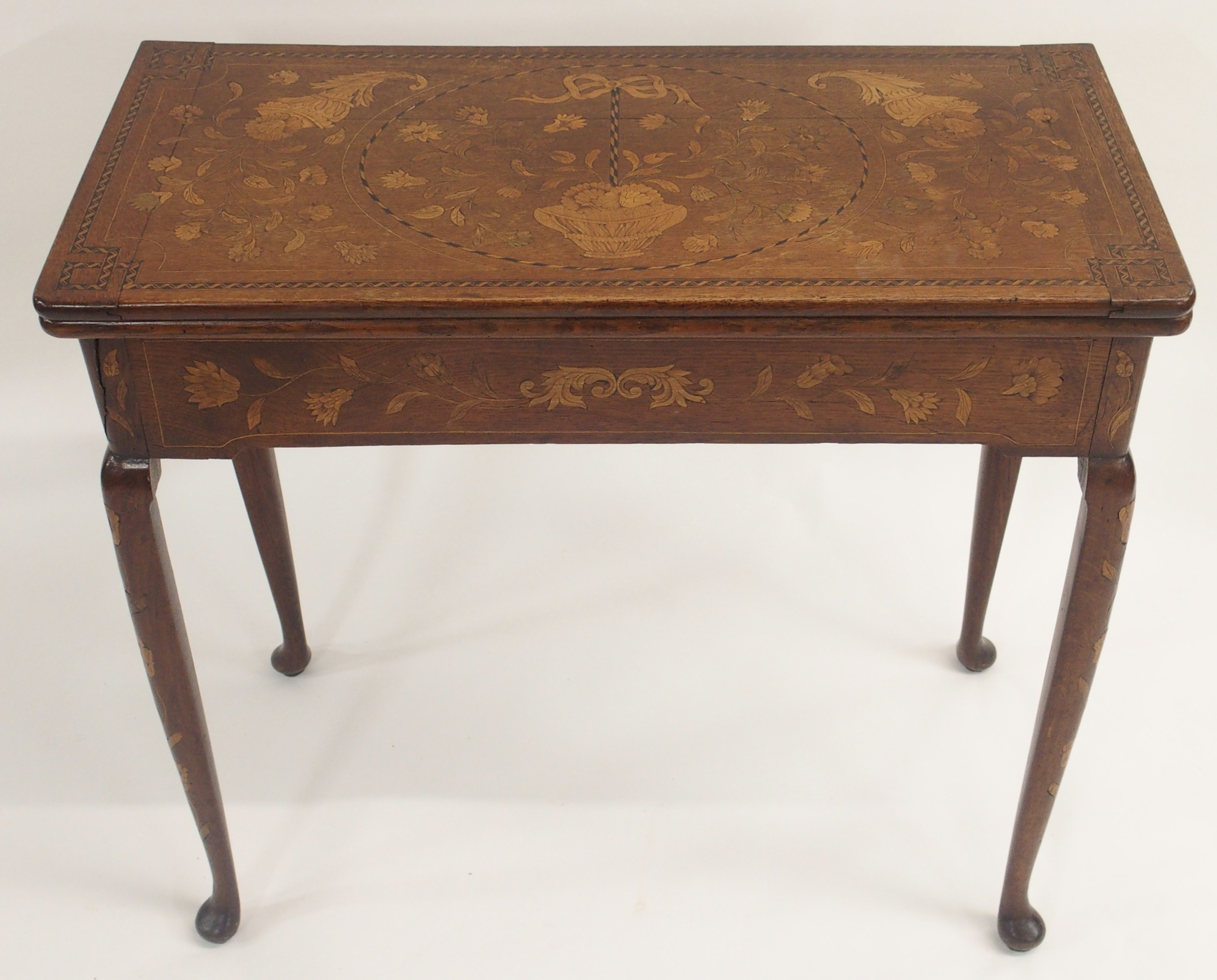 A DUTCH MARQUETRY OAK FOLD OVER CARD TABLE decorated with a basket of ribbon tied flowers,