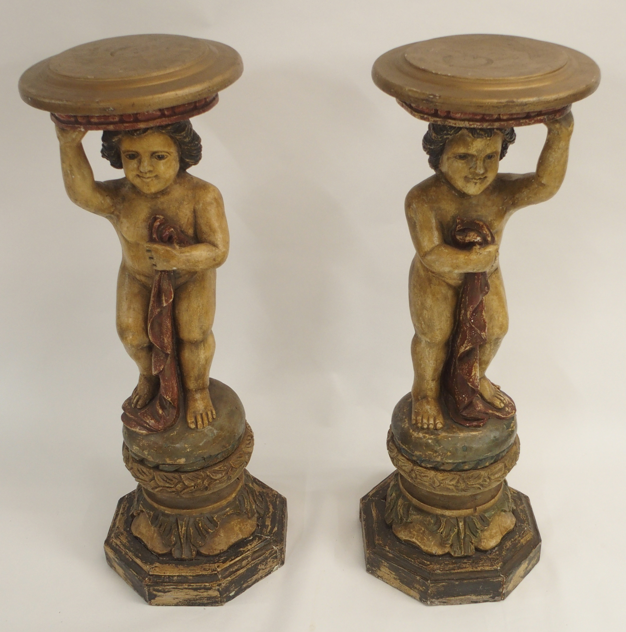 A PAIR OF CONTINENTAL POLYCHROME PINE PEDESTALS each carved with putti holding a robe and standing