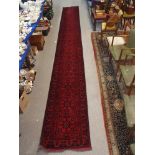 A RED GROUND EASTERN RUNNER with stylised flowers and geometric design, 665cm x 78cm Condition