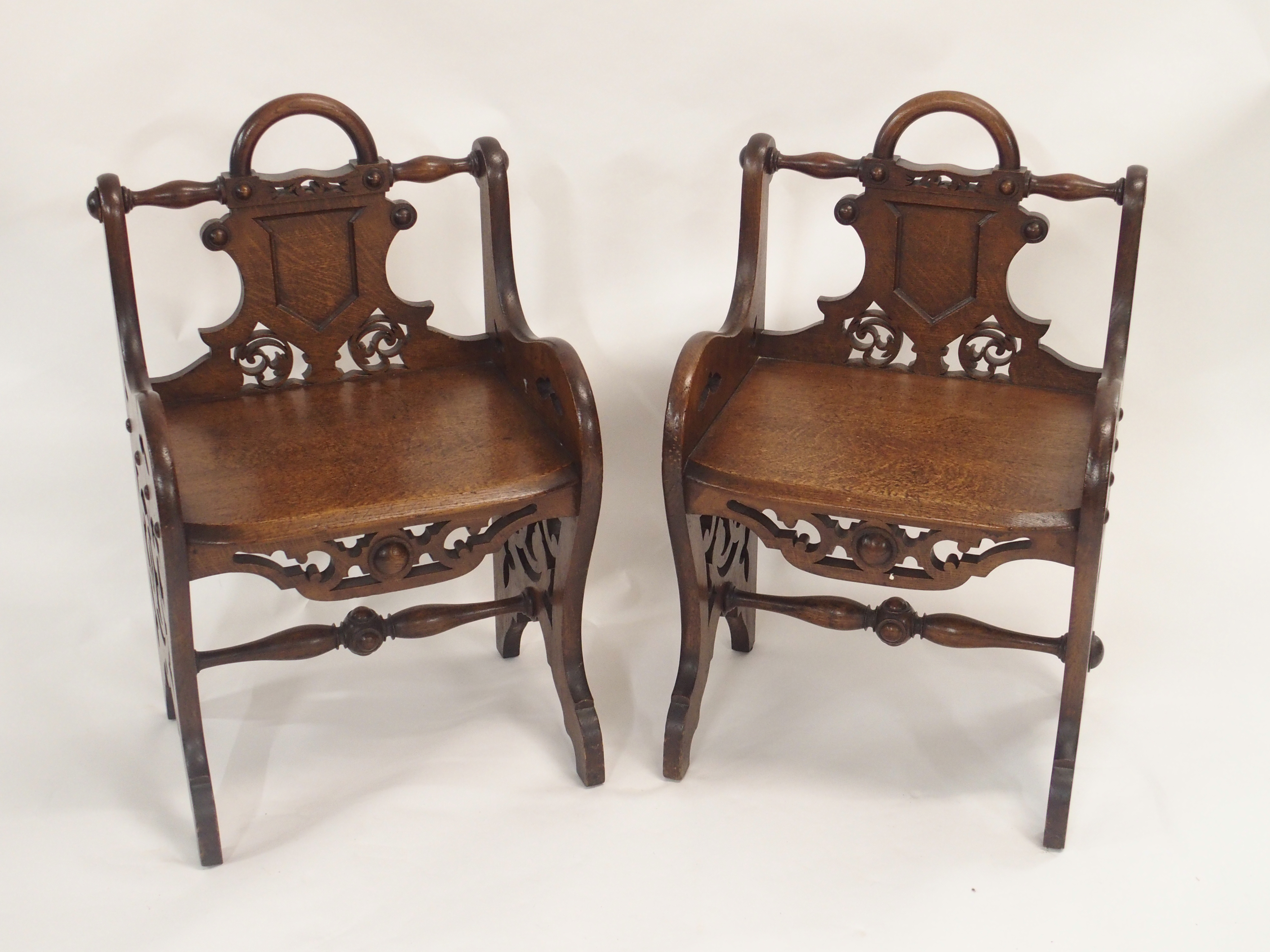 A PAIR OF VICTORIAN OAK HALL CHAIRS each carved with a shield back and pierced scrolls with loop