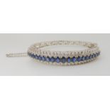 AN 18K WHITE GOLD SAPPHIRE AND DIAMOND BANGLE set with twenty one oval sapphires tapering in size