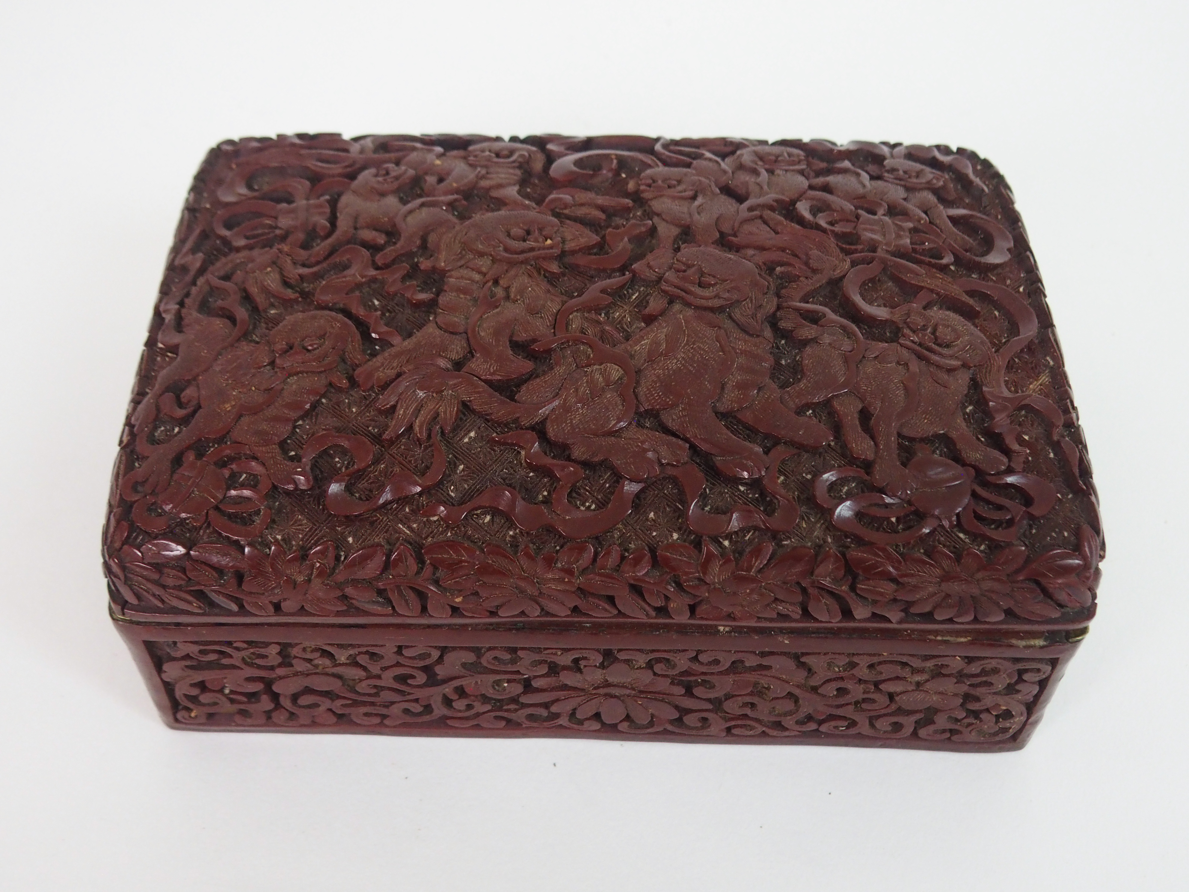 A CHINESE CINNABAR BOX AND COVER carved with kylin with precious objects and ribbons, above