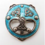 A SILVER AND ENAMEL ALEXANDER RITCHIE BROOCH mythical beasts and knotwork among turquoise enamel.