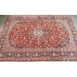 A large red ground Keshan rug with traditional design of blue central medallion, matching