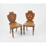 A pair of Victorian oak hall chairs, the pierced backs centred with cartouches, raised on tapering