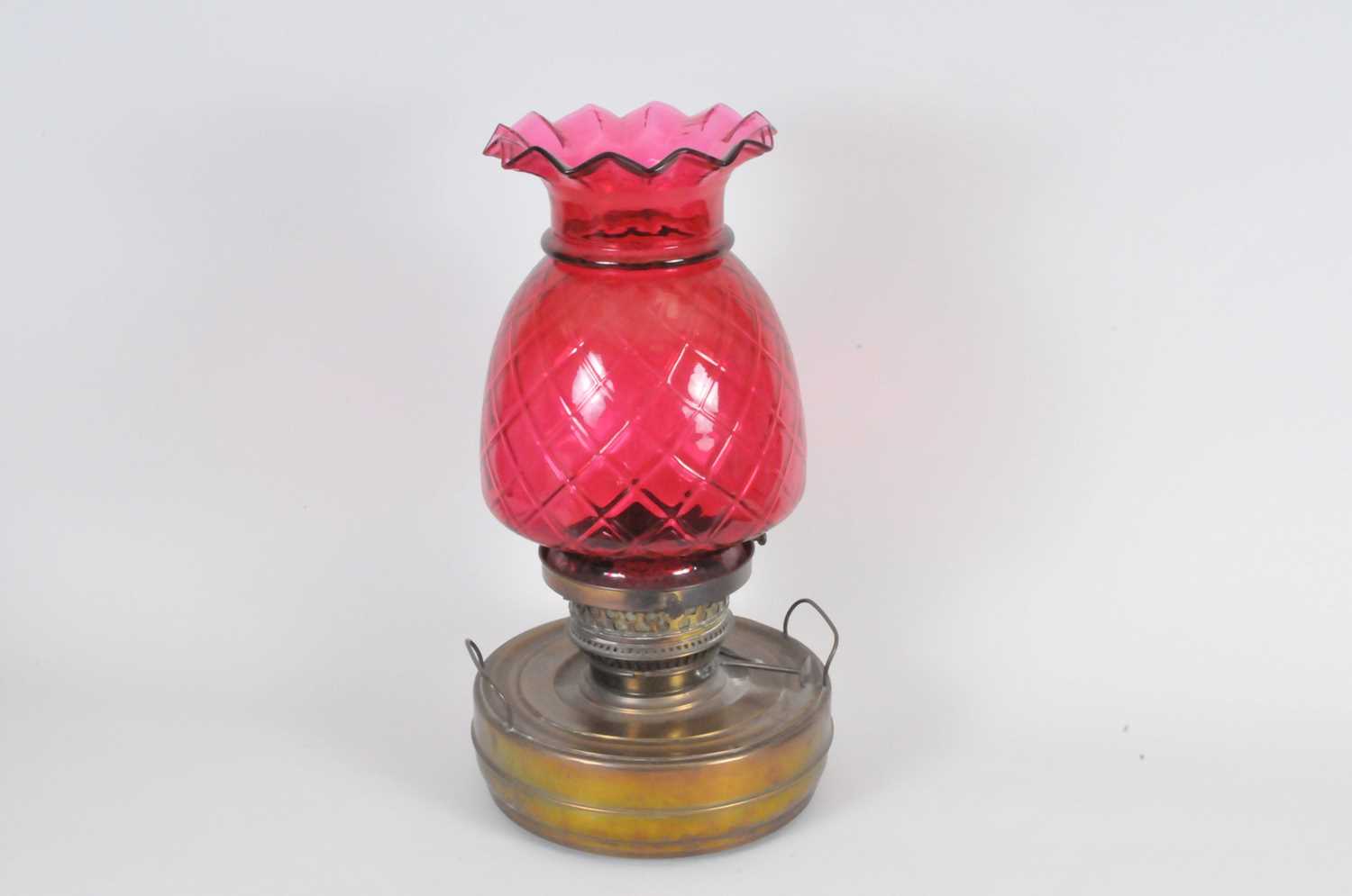 A large brass oil lamp, the cylindrical reservoir below a large pineapple-shaped cranberry glass