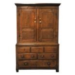 A late 18th century oak livery cupboard with two shaped, panelled doors above three panels, over two