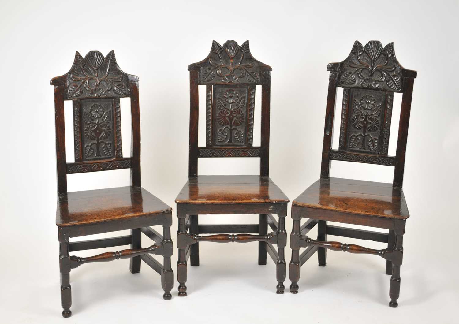 A set of three 17th century oak chairs, each with a foliate carved cresting rail, above a panelled