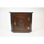 An 18th century hanging corner cupboard, the single panelled door carved with a later arched panel
