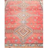 An old eastern woven wool rug, with a red ground and geometric medallions set within alternating