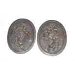 A pair of cast bronze panels of oval form, each decorated with a trio of cherubs, each measuring