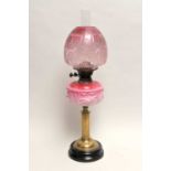 A Victorian oil lamp, with a fluted brass column supporting an opaque cranberry tinted glass