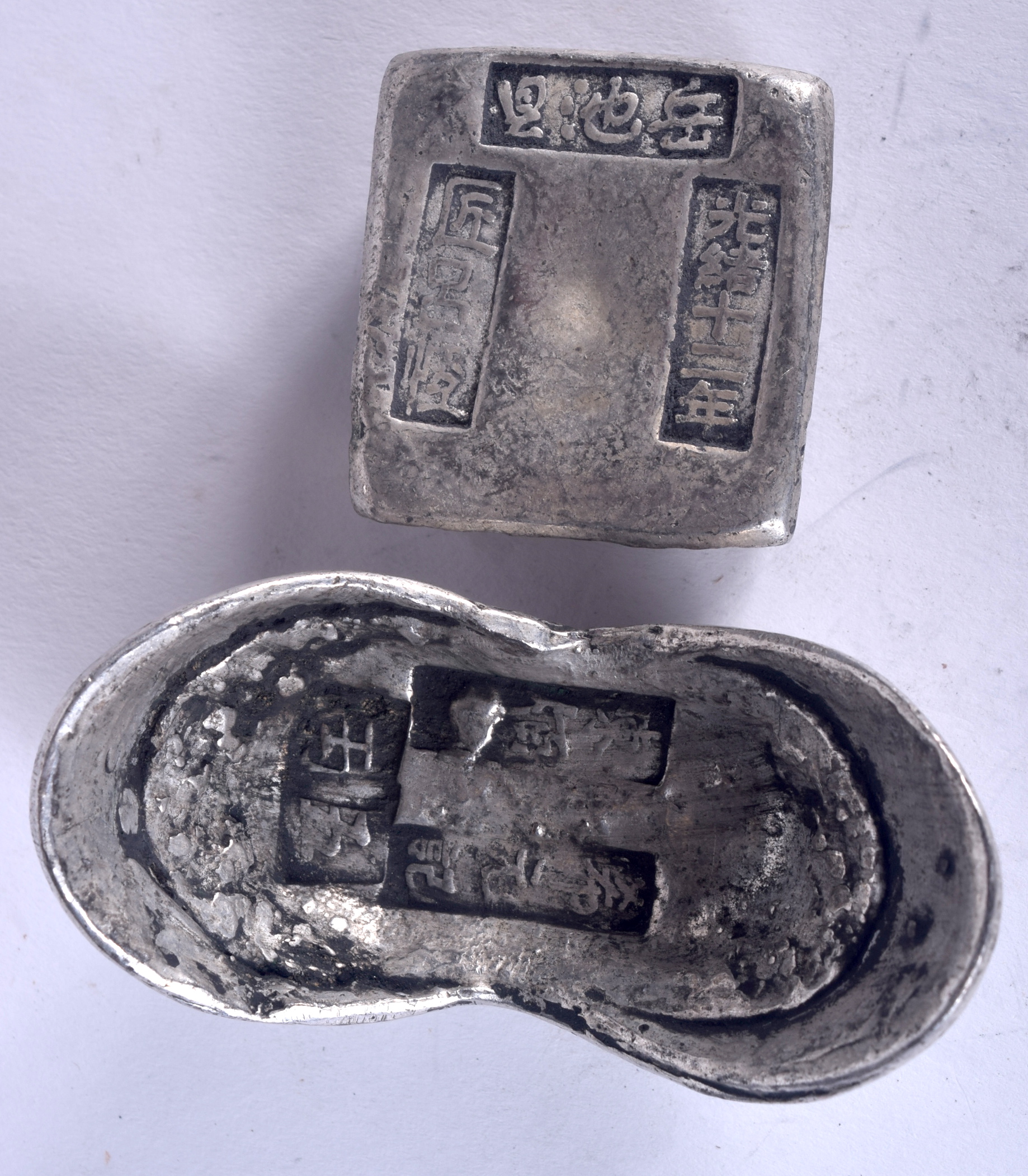 TWO CHINESE WHITE METAL INGOTS, varying form, weight 394 grams. Largest 7.6 cm wide.