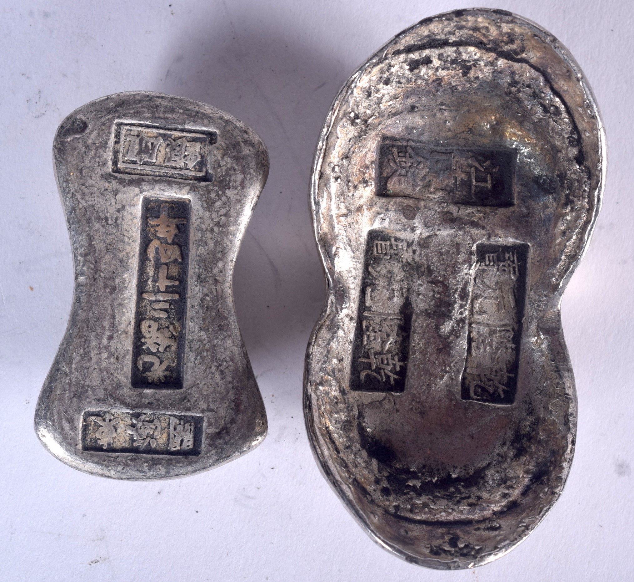 TWO CHINESE WHITE METAL INGOTS, varying form, weight 582 grams. Largest 8.8 cm wide.