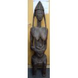 A LARGE AFRICAN CARVED FERTILITY FIGURE, in the form of a seated female holding an infant. 143 cm x